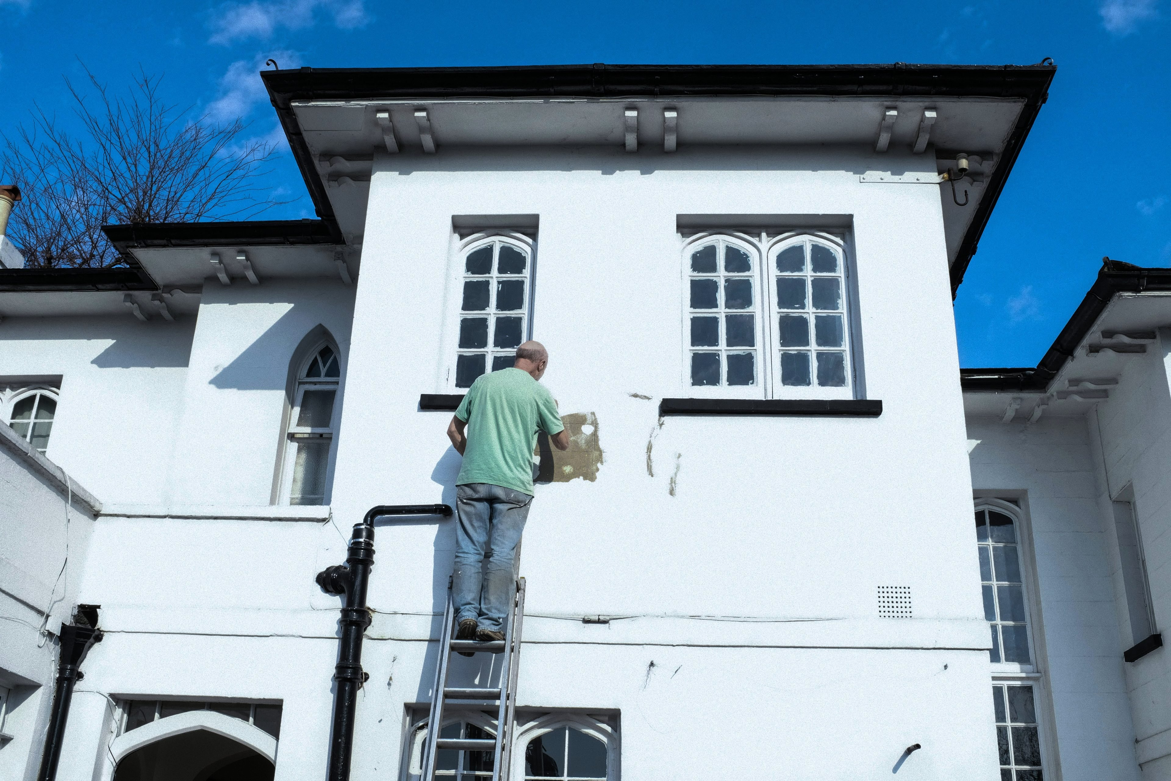 En hantverkare på en stege lagar och målar fasaden på ett vitt hus